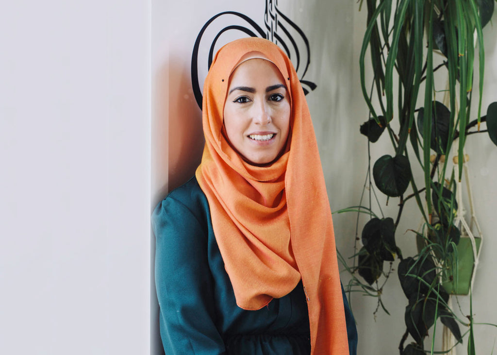 Aseel Tayah in an orange hijab against a white wall for Lunch Lady Magazine