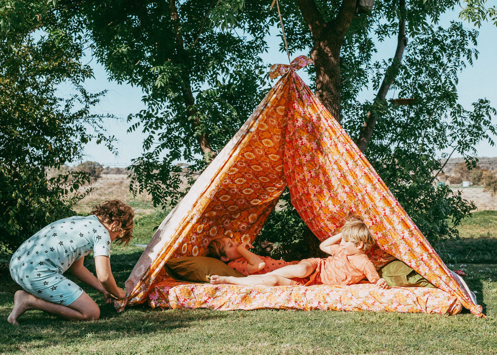 a photo of two kids in a tent made of Beddie sheets in orange for Lunch Lady Magazine
