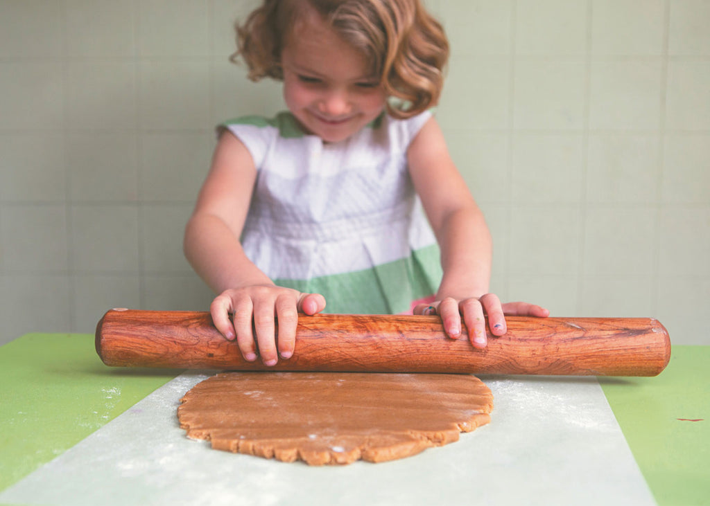 Photo of a young girl using a wooden rolling pin to roll out gingerbread dough