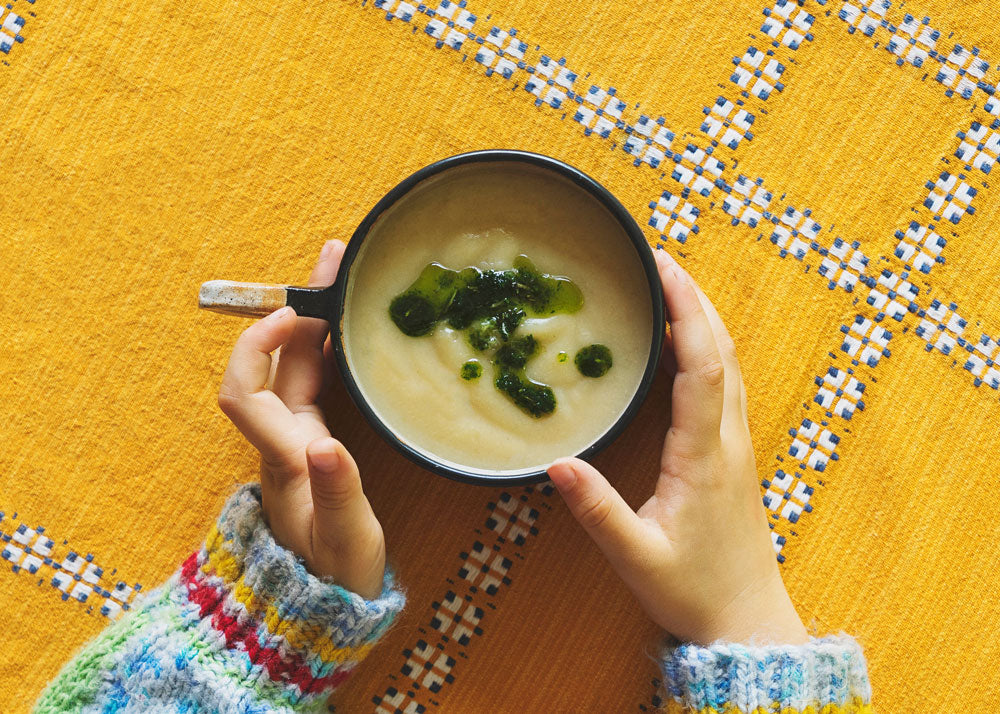 cauliflower and fennel soup with rosemary oil in a large mug with a child's hands holding it
