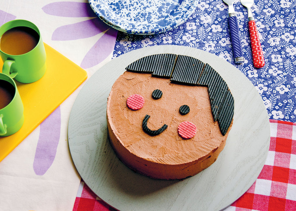 a cake with a happy face on it sits on a round tray on a table with coffee nearby