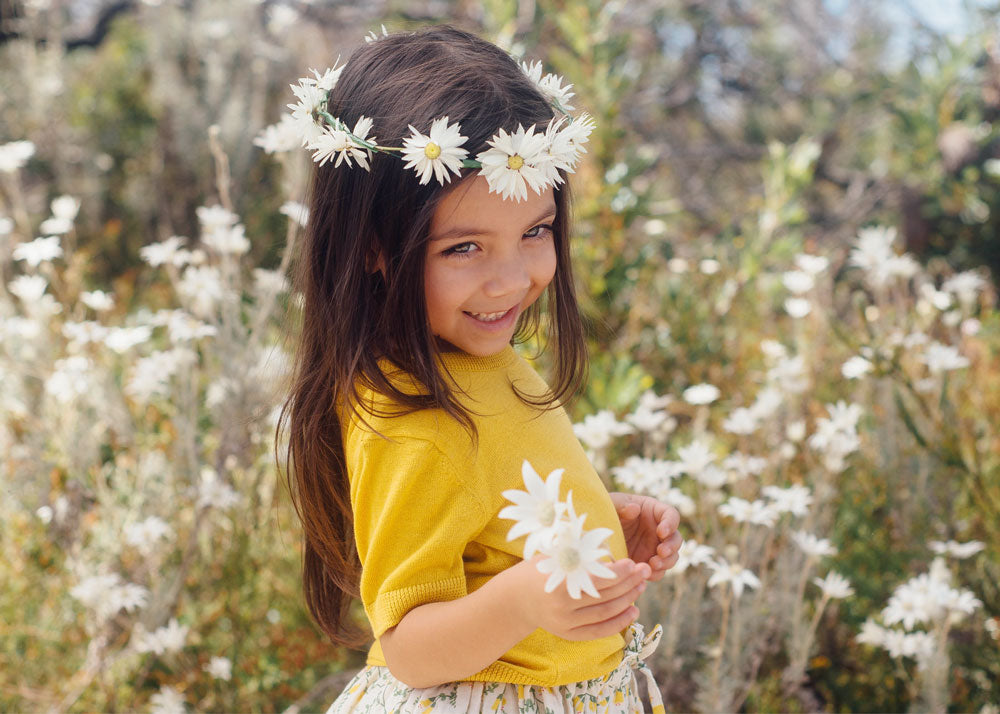 A girl with long dark hair wears a daisy crown while holding flannel flowers