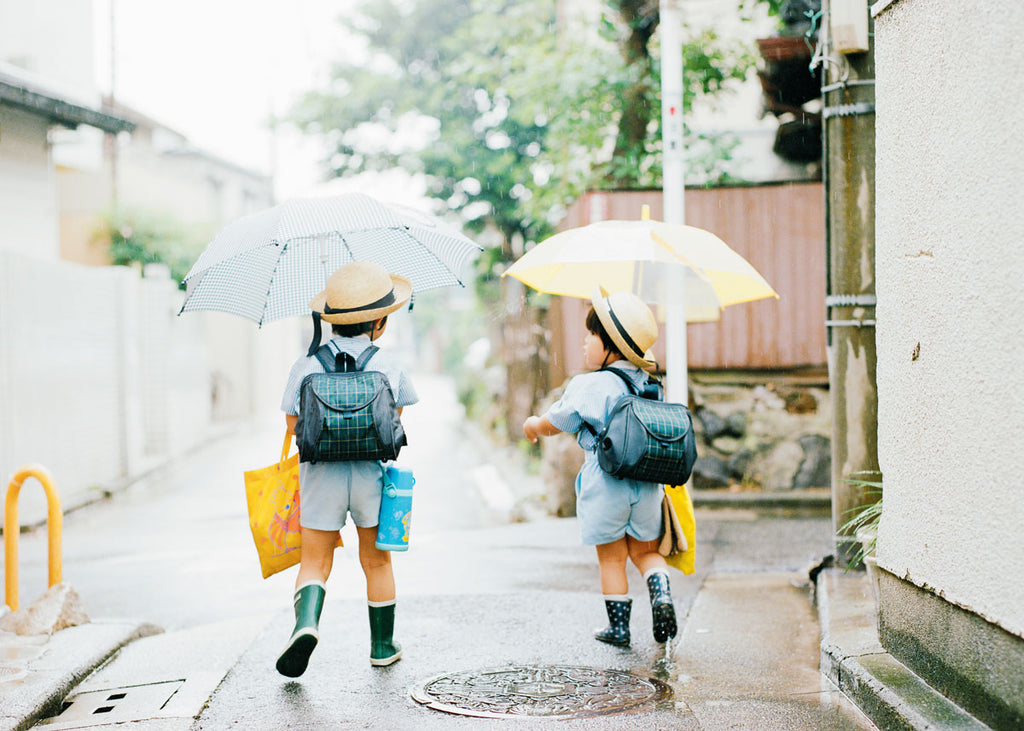 a photo of two japanese school children walking in the rain with umbrellas