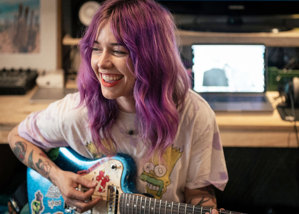 Photo of Nici Ward playing the guitar with purple hair for Lunch Lady Magazine Parents who Play feature
