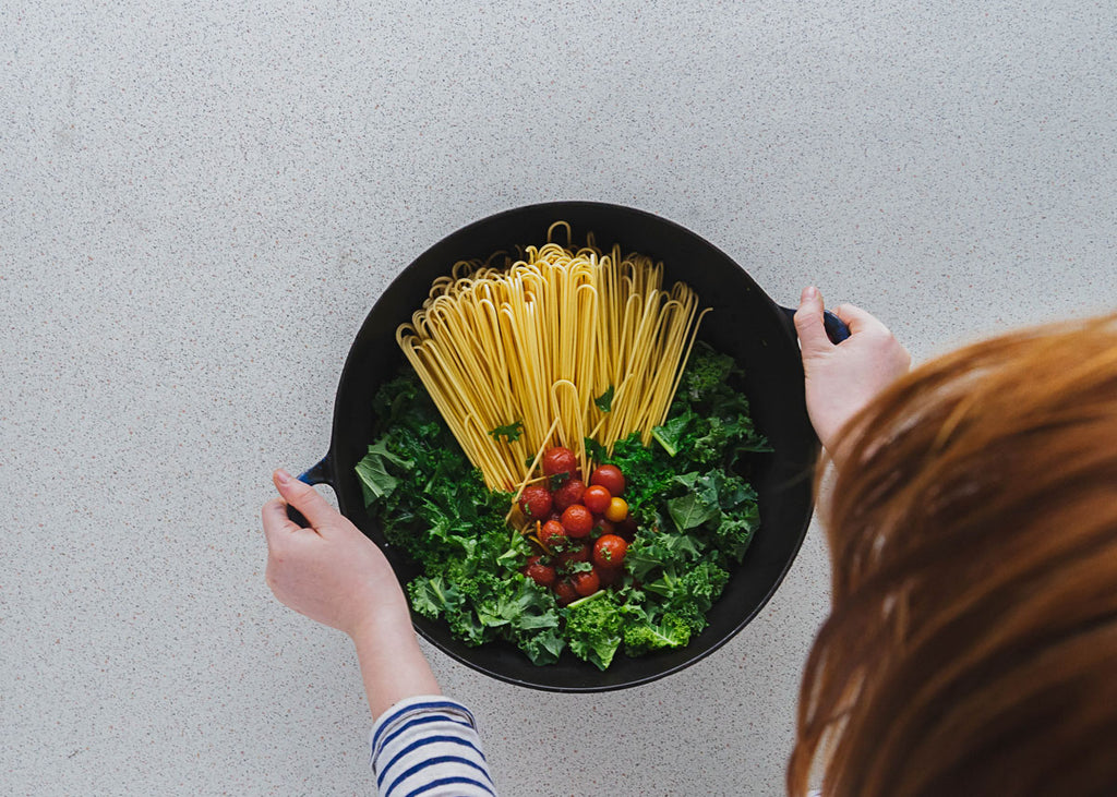 Photo of someone holding a pot with spaghetti, tomatoes and kale in it for Lunch Lady Magazine